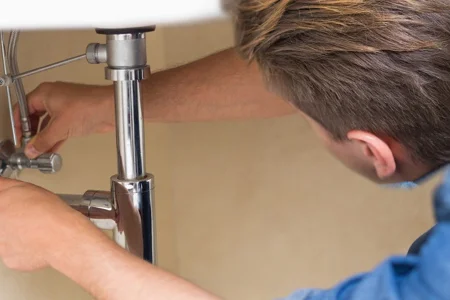 Person repariert Wasserrohre unter Waschbecken